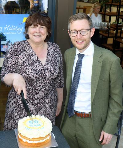 Louise Hillman manager of Keys Holiday Cottages cuts the 50th anniversary cake watched by Duncan Baker MP