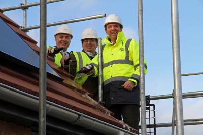 from left Chris Robinson and Sam Coster join Tony Abel on the roof of the new showhome in Hingham to top it out with bottles of The Hops bitter